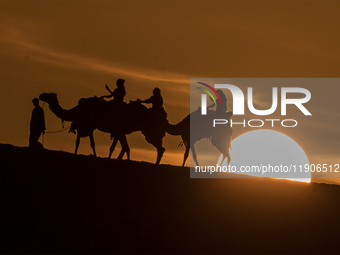 People ride on a camel along the Sealine Sand Dunes against the backdrop of the last sunset of the year 2024 in Sealine, Qatar, on December...