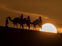 People ride on a camel along the Sealine Sand Dunes against the backdrop of the last sunset of the year 2024 in Sealine, Qatar, on December...