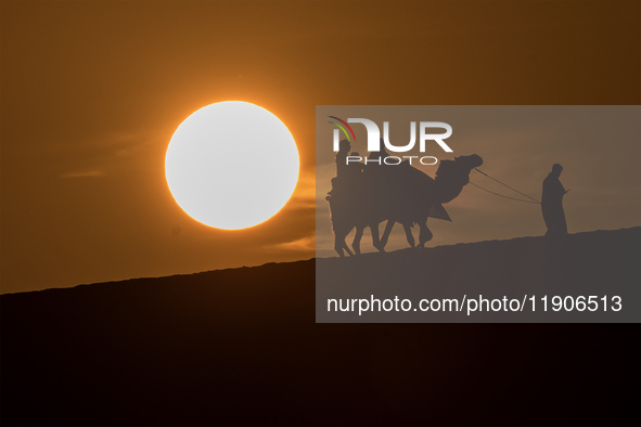 People ride on a camel along the Sealine Sand Dunes against the backdrop of the last sunset of the year 2024 in Sealine, Qatar, on December...