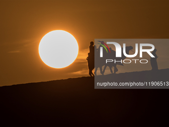 People ride on a camel along the Sealine Sand Dunes against the backdrop of the last sunset of the year 2024 in Sealine, Qatar, on December...