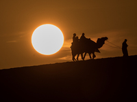 People ride on a camel along the Sealine Sand Dunes against the backdrop of the last sunset of the year 2024 in Sealine, Qatar, on December...