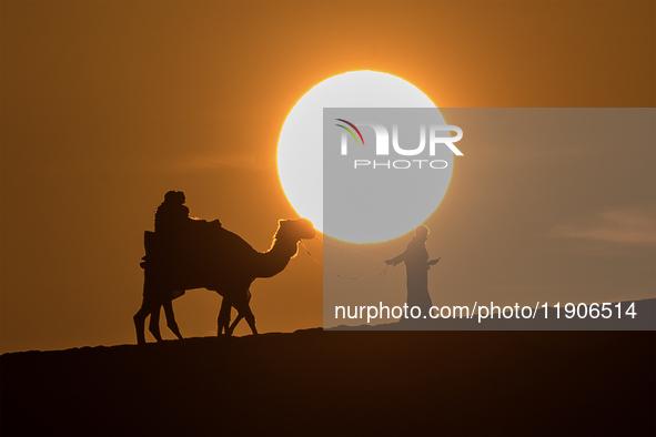 People ride on a camel along the Sealine Sand Dunes against the backdrop of the last sunset of the year 2024 in Sealine, Qatar, on December...