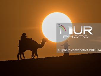 People ride on a camel along the Sealine Sand Dunes against the backdrop of the last sunset of the year 2024 in Sealine, Qatar, on December...