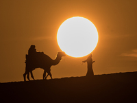 People ride on a camel along the Sealine Sand Dunes against the backdrop of the last sunset of the year 2024 in Sealine, Qatar, on December...