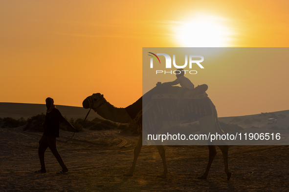 People ride on a camel along the Sealine Sand Dunes against the backdrop of the last sunset of the year 2024 in Sealine, Qatar, on December...