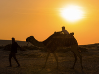 People ride on a camel along the Sealine Sand Dunes against the backdrop of the last sunset of the year 2024 in Sealine, Qatar, on December...