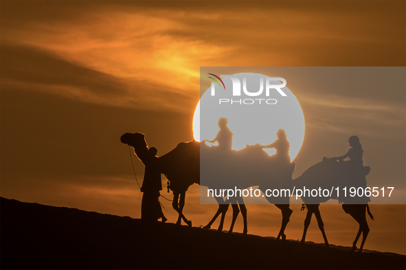 People ride on a camel along the Sealine Sand Dunes against the backdrop of the last sunset of the year 2024 in Sealine, Qatar, on December...