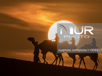 People ride on a camel along the Sealine Sand Dunes against the backdrop of the last sunset of the year 2024 in Sealine, Qatar, on December...