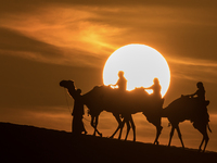 People ride on a camel along the Sealine Sand Dunes against the backdrop of the last sunset of the year 2024 in Sealine, Qatar, on December...