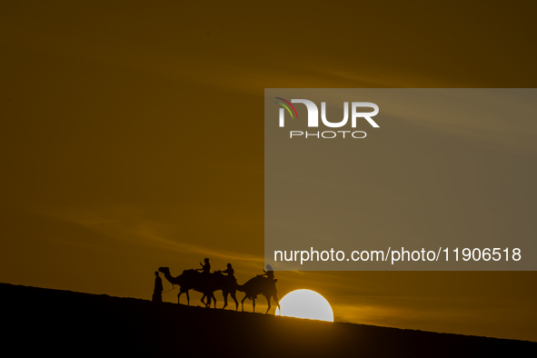 People ride on a camel along the Sealine Sand Dunes against the backdrop of the last sunset of the year 2024 in Sealine, Qatar, on December...