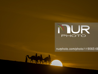 People ride on a camel along the Sealine Sand Dunes against the backdrop of the last sunset of the year 2024 in Sealine, Qatar, on December...