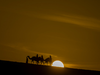 People ride on a camel along the Sealine Sand Dunes against the backdrop of the last sunset of the year 2024 in Sealine, Qatar, on December...