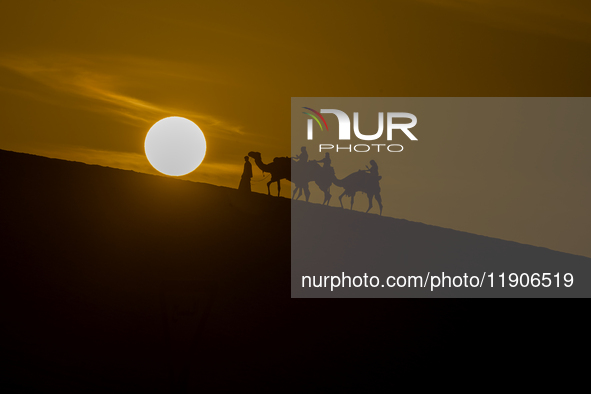 People ride on a camel along the Sealine Sand Dunes against the backdrop of the last sunset of the year 2024 in Sealine, Qatar, on December...