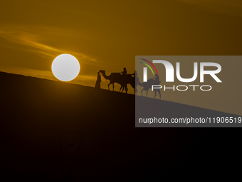 People ride on a camel along the Sealine Sand Dunes against the backdrop of the last sunset of the year 2024 in Sealine, Qatar, on December...