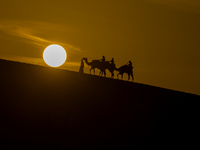 People ride on a camel along the Sealine Sand Dunes against the backdrop of the last sunset of the year 2024 in Sealine, Qatar, on December...