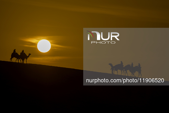 People ride on a camel along the Sealine Sand Dunes against the backdrop of the last sunset of the year 2024 in Sealine, Qatar, on December...