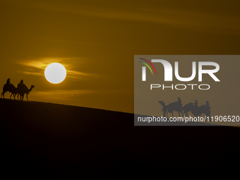 People ride on a camel along the Sealine Sand Dunes against the backdrop of the last sunset of the year 2024 in Sealine, Qatar, on December...