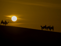 People ride on a camel along the Sealine Sand Dunes against the backdrop of the last sunset of the year 2024 in Sealine, Qatar, on December...