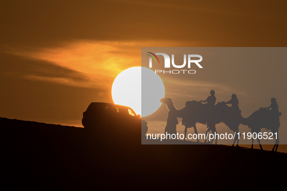 People ride on a camel along the Sealine Sand Dunes against the backdrop of the last sunset of the year 2024 in Sealine, Qatar, on December...