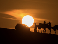 People ride on a camel along the Sealine Sand Dunes against the backdrop of the last sunset of the year 2024 in Sealine, Qatar, on December...