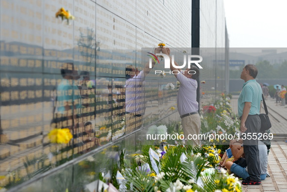 A woman pastes a flower beside the name of her relative killed in the 1976 Tangshan earthquake in front of a memorial wall in Tangshan, nort...