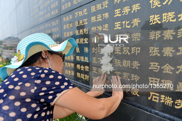 A woman pastes a paper flower beside the name of her relative killed in the 1976 Tangshan earthquake in front of a memorial wall in Tangshan...