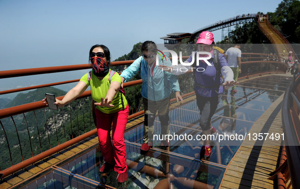 Tourists stretch to walk on a 69-meter-long glass pathway built along the face of a cliff in Shaohuashan national forest park in Weinan City...