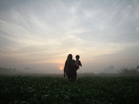 A woman holds her grand daughter walks in the vegetable field during the sun rise outside of Dhaka, Bangladesh on October 25, 2016. Vegetabl...