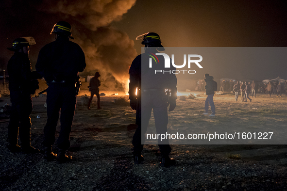 French riot police advance through tear gas and smoke from a fire to disperse migrants throwing stones and lighting fires at the Jungle migr...