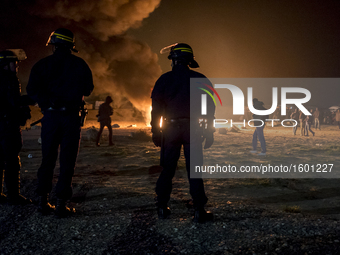 French riot police advance through tear gas and smoke from a fire to disperse migrants throwing stones and lighting fires at the Jungle migr...