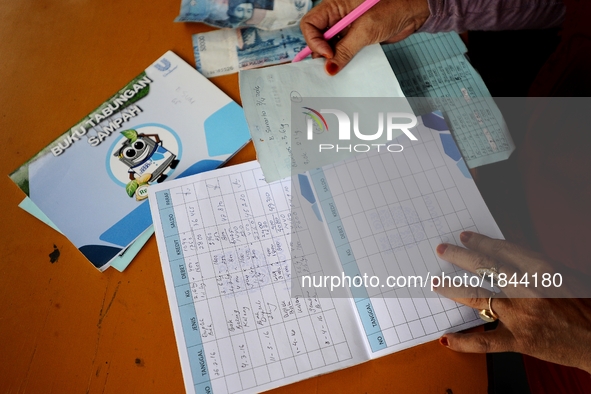 A woman writes on Bank Sampah saving book. 
Bank Sampah (Garbage Bank) is a small business unit in neighborhood community operated by volunt...