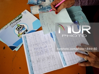 A woman writes on Bank Sampah saving book. 
Bank Sampah (Garbage Bank) is a small business unit in neighborhood community operated by volunt...