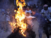 Nepalese devotee swing their child over the burning straw effigy of the demon Ghantakarna during the Gathemangal festival celebrated at Bhak...