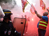 Metalworkers and police officers are surrounded by smoke as they march with banners and flags in the streets of Paris on October 13, 2017. S...