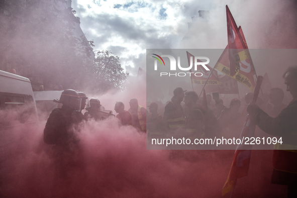 Metalworkers and police officers are surrounded by smoke as they march with banners and flags in the streets of Paris on October 13, 2017. S...