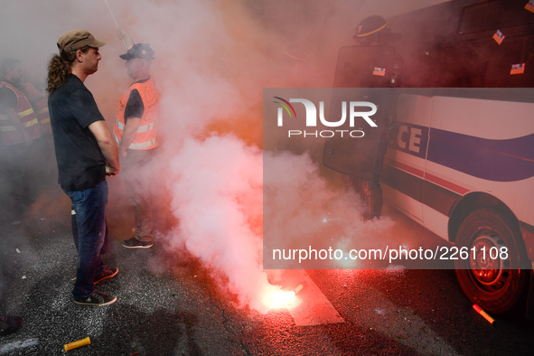 Metalworkers and police officers are surrounded by smoke as they march with banners and flags in the streets of Paris on October 13, 2017. S...