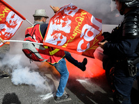 Metalworkers and police officers are surrounded by smoke as they march with banners and flags in the streets of Paris on October 13, 2017. S...