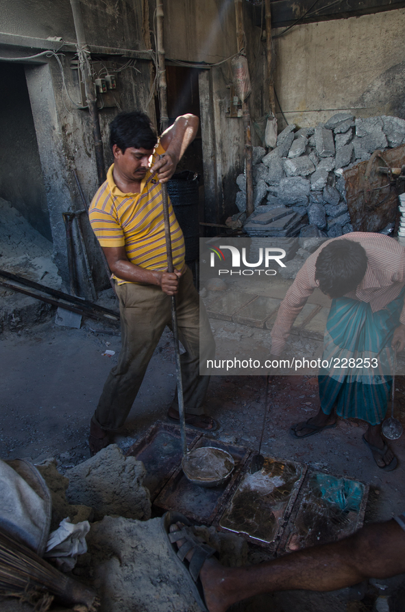 DHAKA, BANGLADESH. Juli  2013.  Two men fill the bar mold's with melt lead, without any safety protection. Bangladesh has one of the highest...