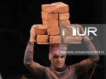 Indian Labour carries pile of bricks on his head near a construction site at Gurugram, Haryana on 16th December 2017. (