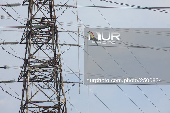 Workers assemble cables in high-voltage power towers without adequate safety equipment, even among them seen wearing only shorts and not wea...