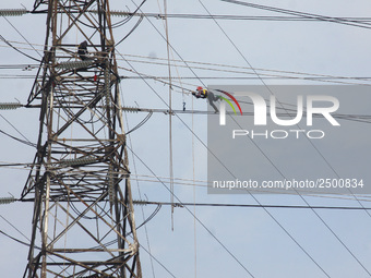 Workers assemble cables in high-voltage power towers without adequate safety equipment, even among them seen wearing only shorts and not wea...