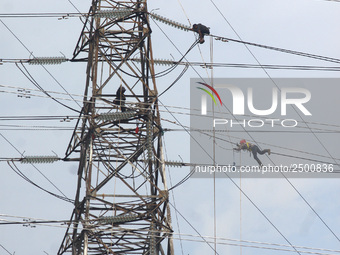 Workers assemble cables in high-voltage power towers without adequate safety equipment, even among them seen wearing only shorts and not wea...