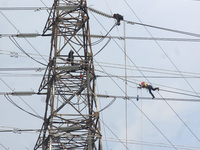 Workers assemble cables in high-voltage power towers without adequate safety equipment, even among them seen wearing only shorts and not wea...