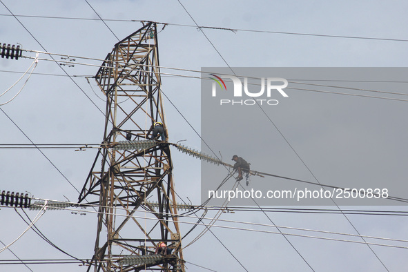 Workers assemble cables in high-voltage power towers without adequate safety equipment, even among them seen wearing only shorts and not wea...