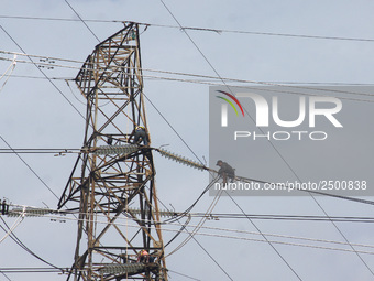 Workers assemble cables in high-voltage power towers without adequate safety equipment, even among them seen wearing only shorts and not wea...