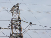 Workers assemble cables in high-voltage power towers without adequate safety equipment, even among them seen wearing only shorts and not wea...