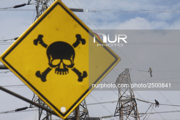 Workers assemble cables in high-voltage power towers without adequate safety equipment, even among them seen wearing only shorts and not wea...