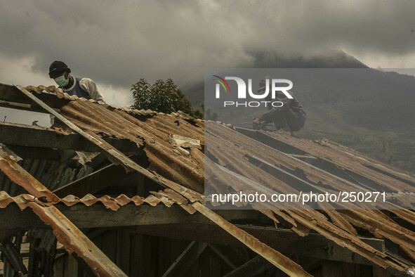 A Worker repair a damaged school building as Mount Sinabung is seen on the background in Sigarang garang village, North Sumatra, Indonesia,...