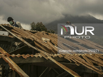 A Worker repair a damaged school building as Mount Sinabung is seen on the background in Sigarang garang village, North Sumatra, Indonesia,...