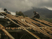 A Worker repair a damaged school building as Mount Sinabung is seen on the background in Sigarang garang village, North Sumatra, Indonesia,...